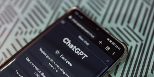 Smartphone with ChatGPT app interface next to eyeglasses on patterned surface.