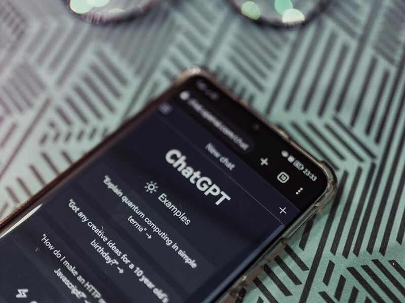 Smartphone with ChatGPT app interface next to eyeglasses on patterned surface.