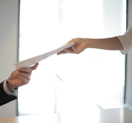 Close-up of hands exchanging documents in a business setting indoors.