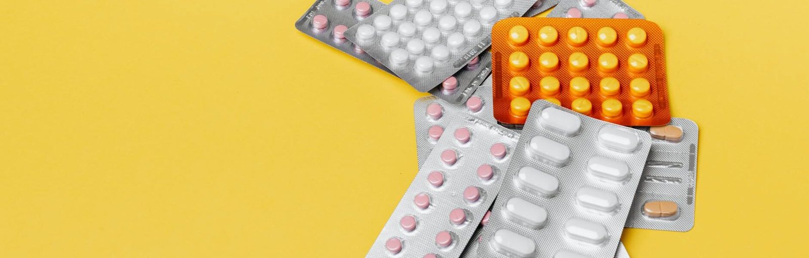 heap of various pills in blisters on yellow background